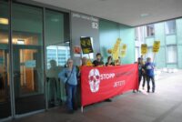 Vor dem Hauptsitz von Bayer Cropscience in Basel stehen Protestierende mit Schildern und mit einem roten Banner. Auf dem Banner ist "Stopp Glyphosat Jetzt" zu lesen